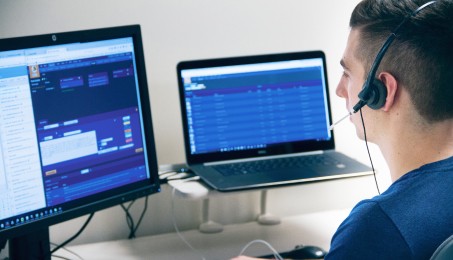 Man wearing a headset, facing two computer screens.